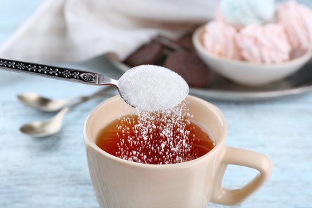 Adding sugar to cup of black tea on wooden tableの写真素材
