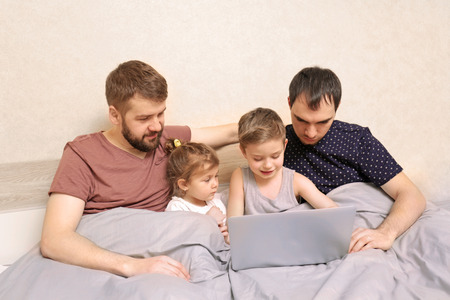 Male gay couple with children resting in bed at home