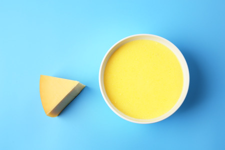 Bowl with tasty cheese sauce on color background