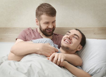 Happy gay couple hugging in bed at homeの写真素材