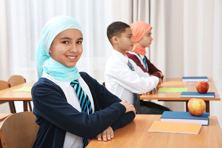 Cute girl sitting at desk in school classの写真素材