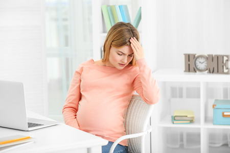 Pregnant woman suffering from headaches while sitting at workplace in officeの写真素材
