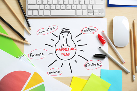 Paper sheet with text MARKETING PLAN on table