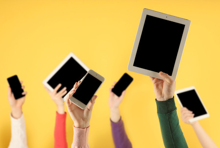 Young people raising hands with digital devices on color background