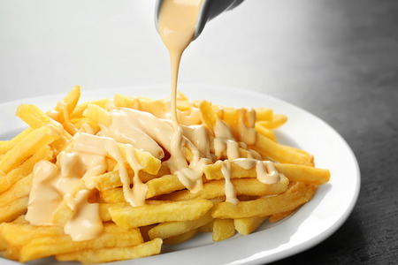 Pouring cheese sauce on french fries, closeupの写真素材