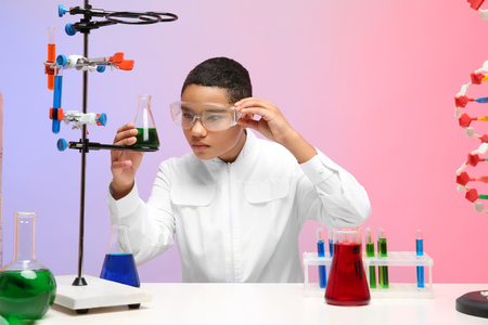 School boy sitting at workplace and controlling experiment in chemistry classの写真素材