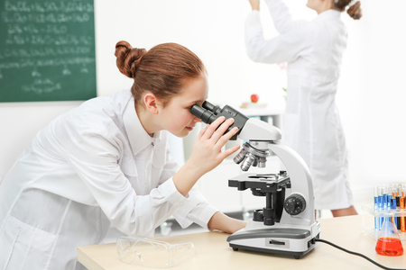 Beautiful school girl looking through microscope in chemistry classの写真素材