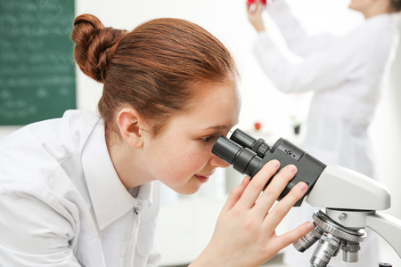 Beautiful school girl looking through microscope in chemistry classの写真素材