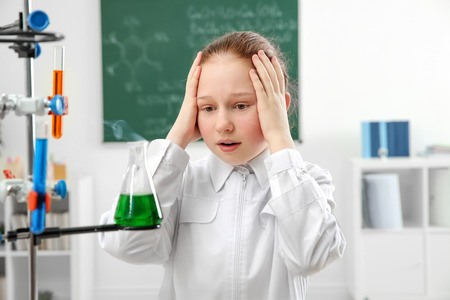Excited beautiful school girl looking at flask in chemistry classの写真素材