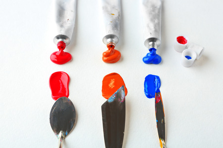 Tubes with oil paints and palette knives on white paper background