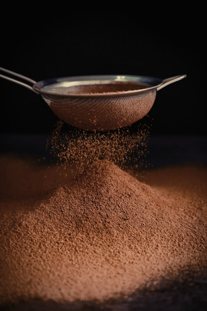 Sieve and powdered cocoa on black backgroundの写真素材