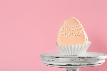 Dessert stand with creative egg shape Easter cookies on pink background
