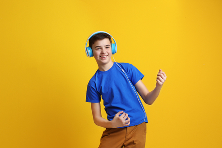 Teenager with headphones listening to music on color background