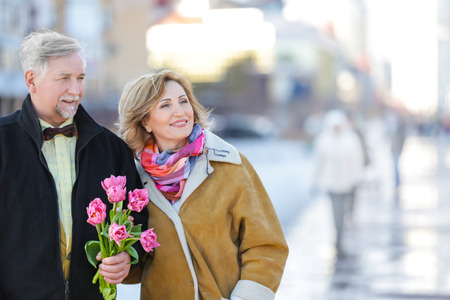 Happy senior couple with bouquet of flowers  on a walkの写真素材