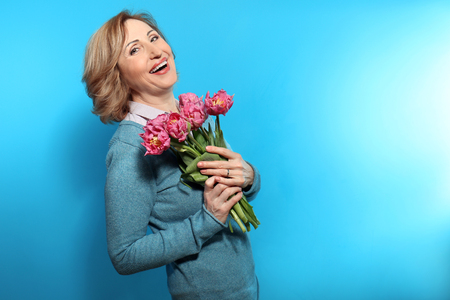 Happy senior woman with bouquet of flowers on color backgroundの写真素材