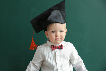 Cute little boy with magister hat and blackboard on backgroundの写真素材