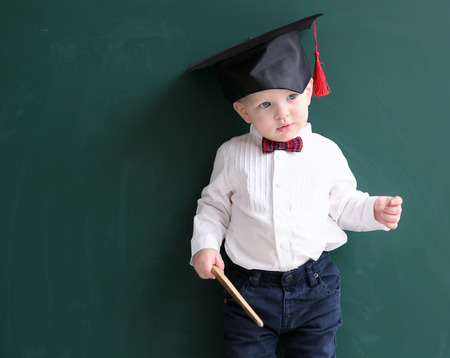 Cute little boy with pointer and magister hat near blackboardの写真素材