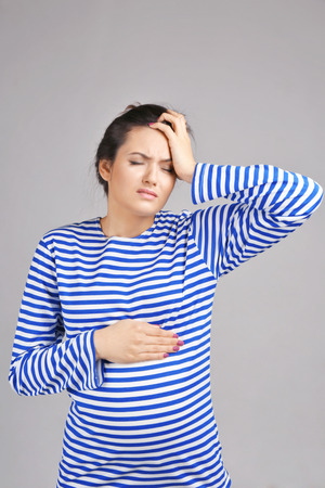 Young pregnant woman suffering from headache on grey backgroundの写真素材