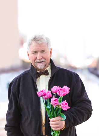 Happy senior man with bouquet of flowers outdoorsの写真素材