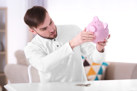 Young man sitting at table with piggy bankの写真素材