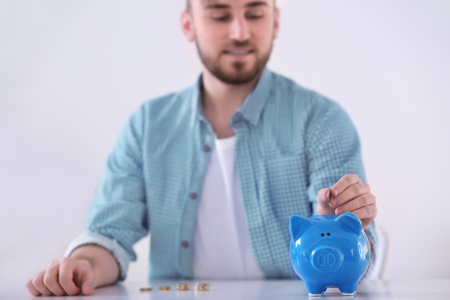 Man sitting at table and putting coin into piggy bank on light backgroundの写真素材
