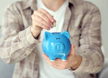 Man putting coin into piggy bank, closeup