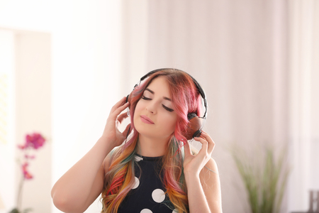Young woman with colorful dyed hair listening to music at homeの写真素材