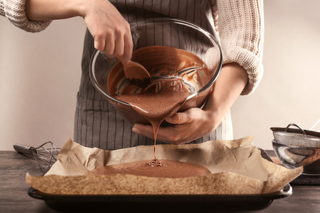 Woman pouring cacao liquid dough into baking trayの写真素材