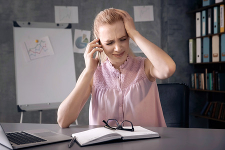 Beautiful young woman suffering from headache while working in officeの写真素材