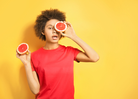 Beautiful African girl with sliced grapefruit on yellow backgroundの写真素材