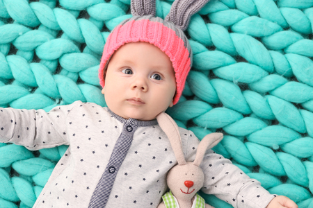 Cute little baby in bunny hat lying on soft knitted blanketの写真素材