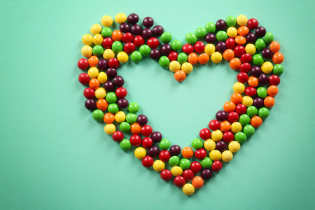 Colorful candies in shape of heart on color background