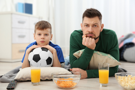 Father and son watching football on TV at homeの写真素材