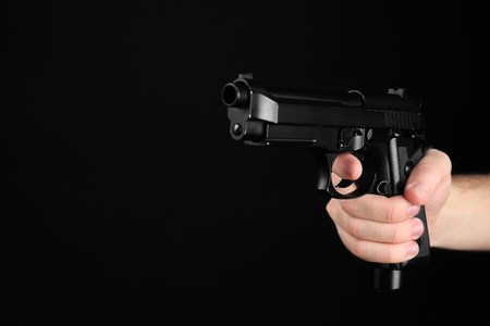 Male hand holding gun on black background