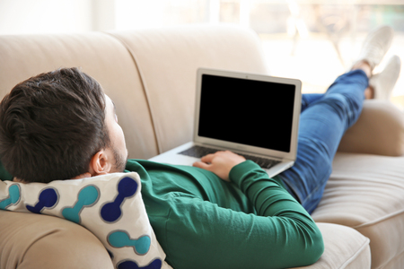 Happy young man lying on sofa with laptopの写真素材