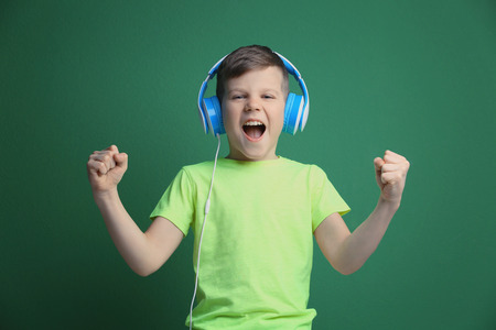Cute little boy in headphones listening to music on color background