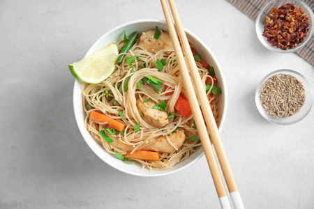 Delicious rice noodle in white plate with spices on light background