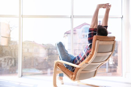 Happy young man sitting in armchair and stretching himselfの写真素材