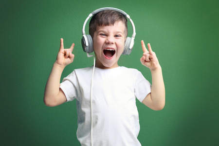 Cute little boy in headphones listening to music on color backgroundの写真素材