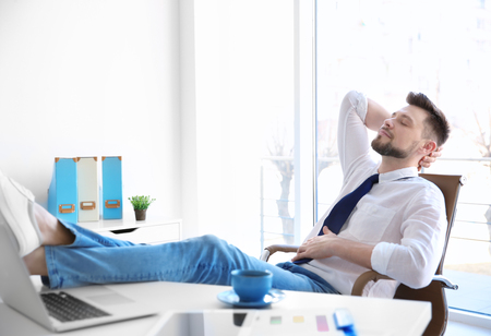 Young businessman relaxing at workplace with his feet on deskの写真素材