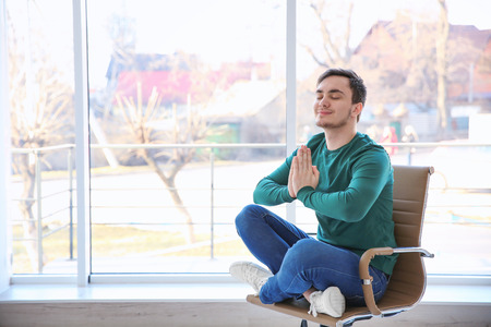 Happy young man sitting on chair and meditatingの写真素材
