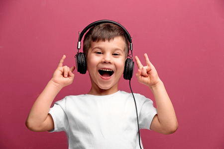 Cute little boy in headphones listening to music on color backgroundの写真素材