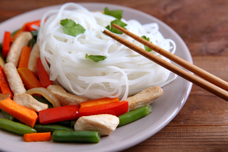 Plate with tasty rice noodle and vegetables on wooden tableの写真素材