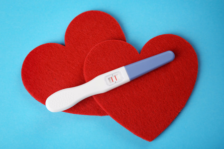 Pregnancy test and red hearts on color backgroundの写真素材