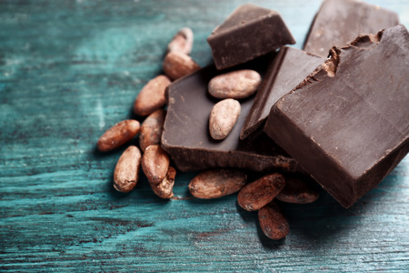 Broken chocolate pieces and cocoa beans on color backgroundの写真素材