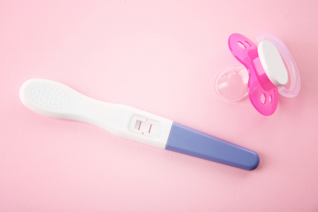 Pregnancy test and pacifier on pink background. Baby born conceptの写真素材