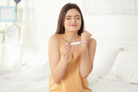 Happy young woman waiting for pregnancy test results in bedroomの写真素材