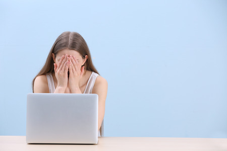 Beautiful young woman suffering from headache while working with laptop, on color background