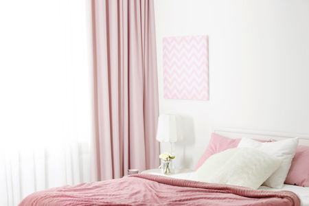 Comfortable bed with soft pink coverlet and pillows in light modern roomの写真素材