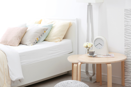 Comfortable bed with soft beige coverlet and pillows in light modern roomの写真素材